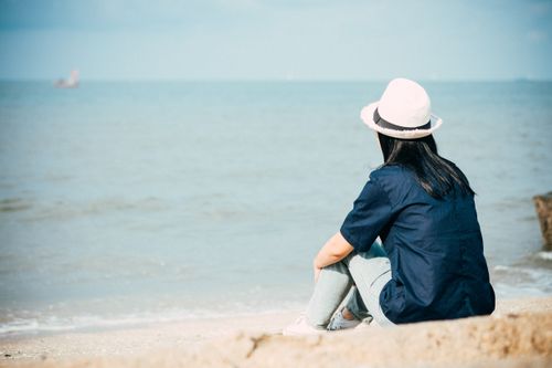Free A woman sits peacefully by the ocean in summer, enjoying serene beach views. Stock Photo
