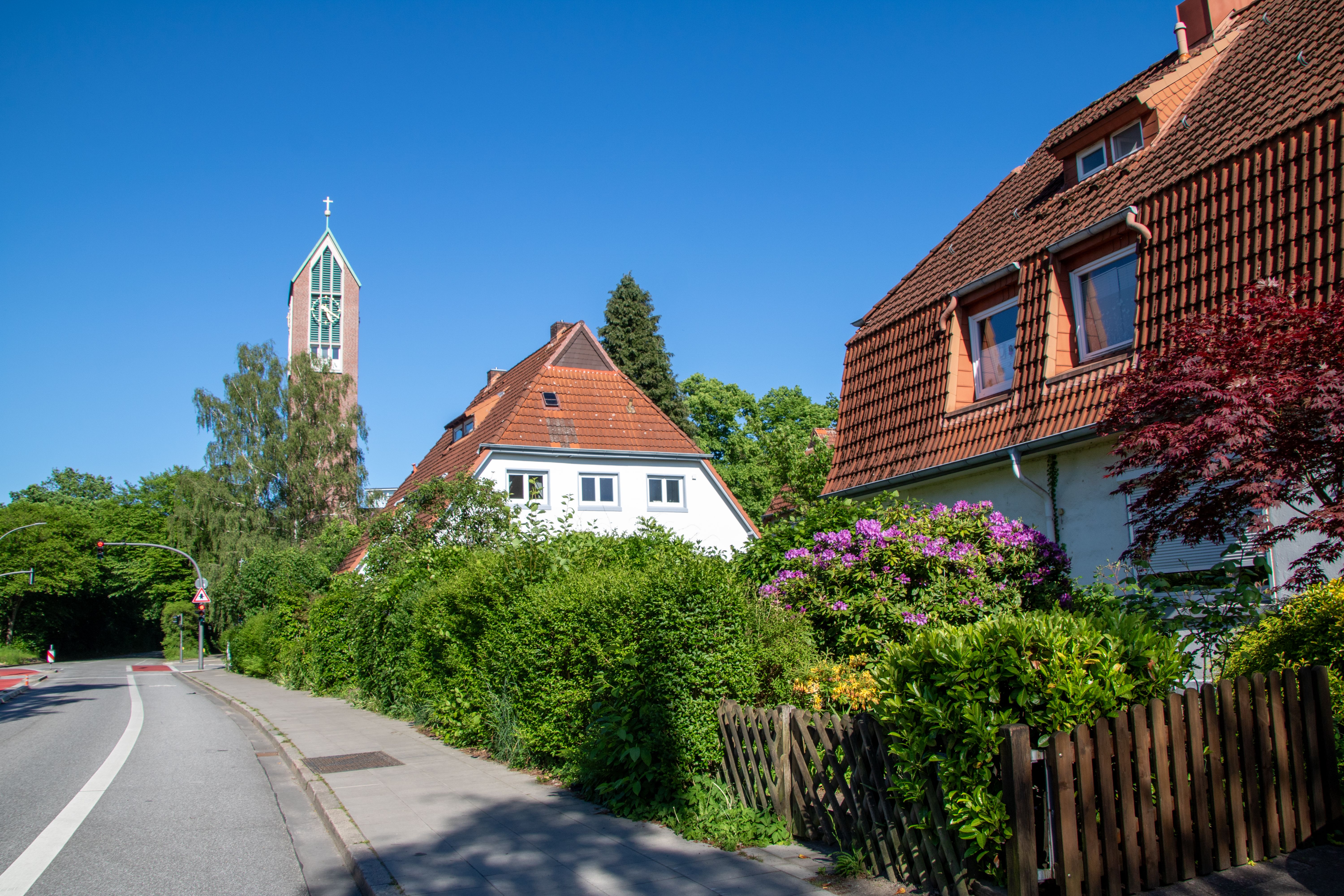 Picturesque residential street in Hamburg with a church tower and lush greenery.