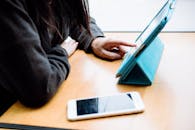 一个人正与桌上的平板电脑互动，旁边的智能手机展示了现代数字习惯