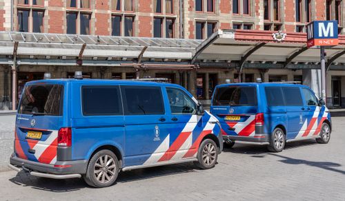 Free Two blue police vans parked outside a European train station on a sunny day. Stock Photo