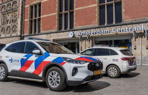 Free Police cars parked in front of Amsterdam Centraal Station on a sunny day. Stock Photo