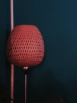 Stylish woven lamp against a dark teal wall, perfect for modern interior decor.