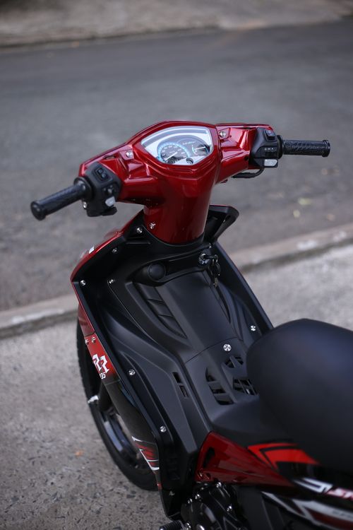 Free Close-up of a red scooter handlebar parked on a city street highlighting modern design. Stock Photo