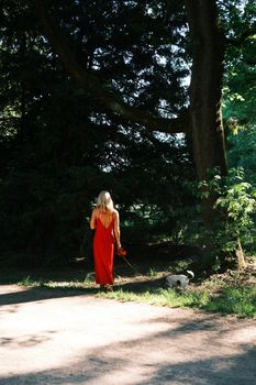 A woman in a red dress walks her dog in a lush Munich park, capturing a serene summer scene.