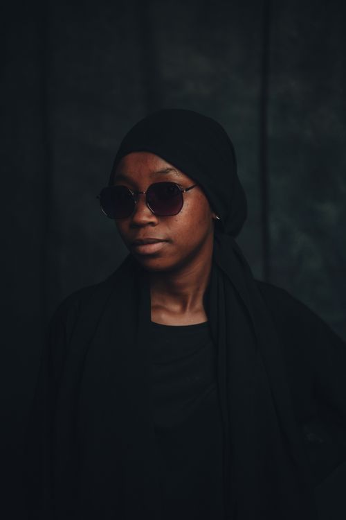 Free Sophisticated portrait of a woman in sunglasses wearing dark attire with a moody backdrop. Captured in Nigeria. Stock Photo