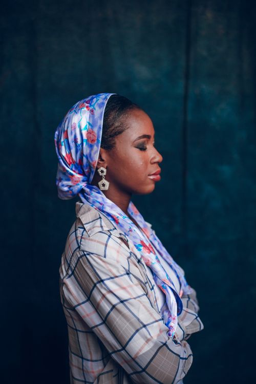 Free Profile portrait of an elegant Nigerian woman wearing a vibrant floral headscarf against a dark background. Stock Photo