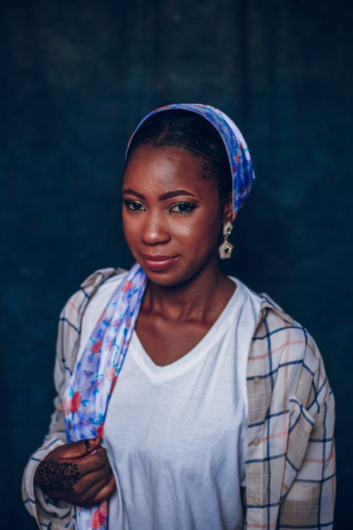 Free A beautiful Nigerian woman poses confidently wearing a colorful headscarf and patterned shirt against a dark backdrop. Stock Photo