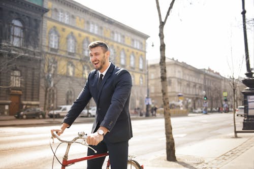 Мужчина в черном пиджаке и черных штанах едет на красном велосипеде