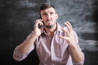 成年男子穿着粉红色礼服衬衫，在室内用智能手机交谈，显得很突出