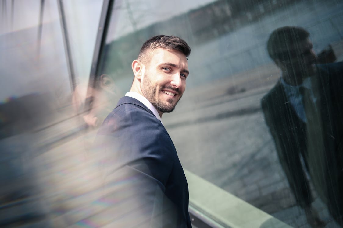 Free Cheerful businessman in formal wear standing in front of glass wall Stock Photo