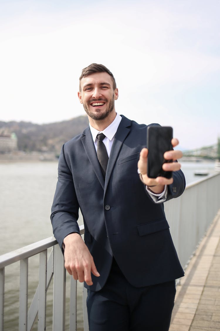 Man In Black Suit Jacket Holding Black Smartphone