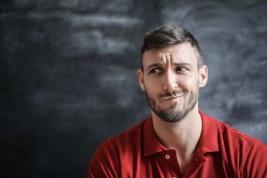 A playful, expressive portrait of a bearded man in a red polo shirt with a chalkboard background.