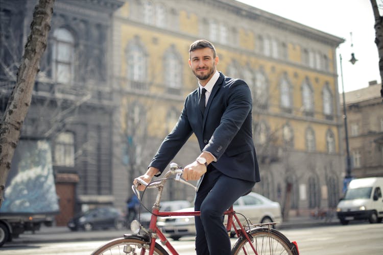 Man In Black Suit Jacket And Black Pants While Riding A Red Bicycle