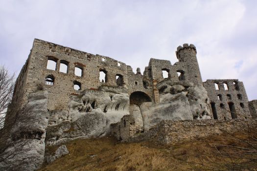 Old stone castle ruin showing weathered walls and turrets under a cloudy sky.