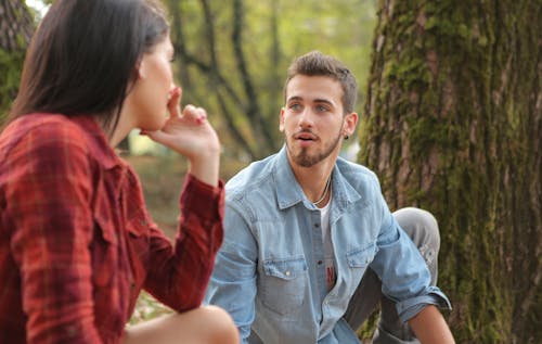 Uomo In Denim Blu Abbottonare La Camicia Che Si Siede Accanto Alla Donna Vicino All'albero