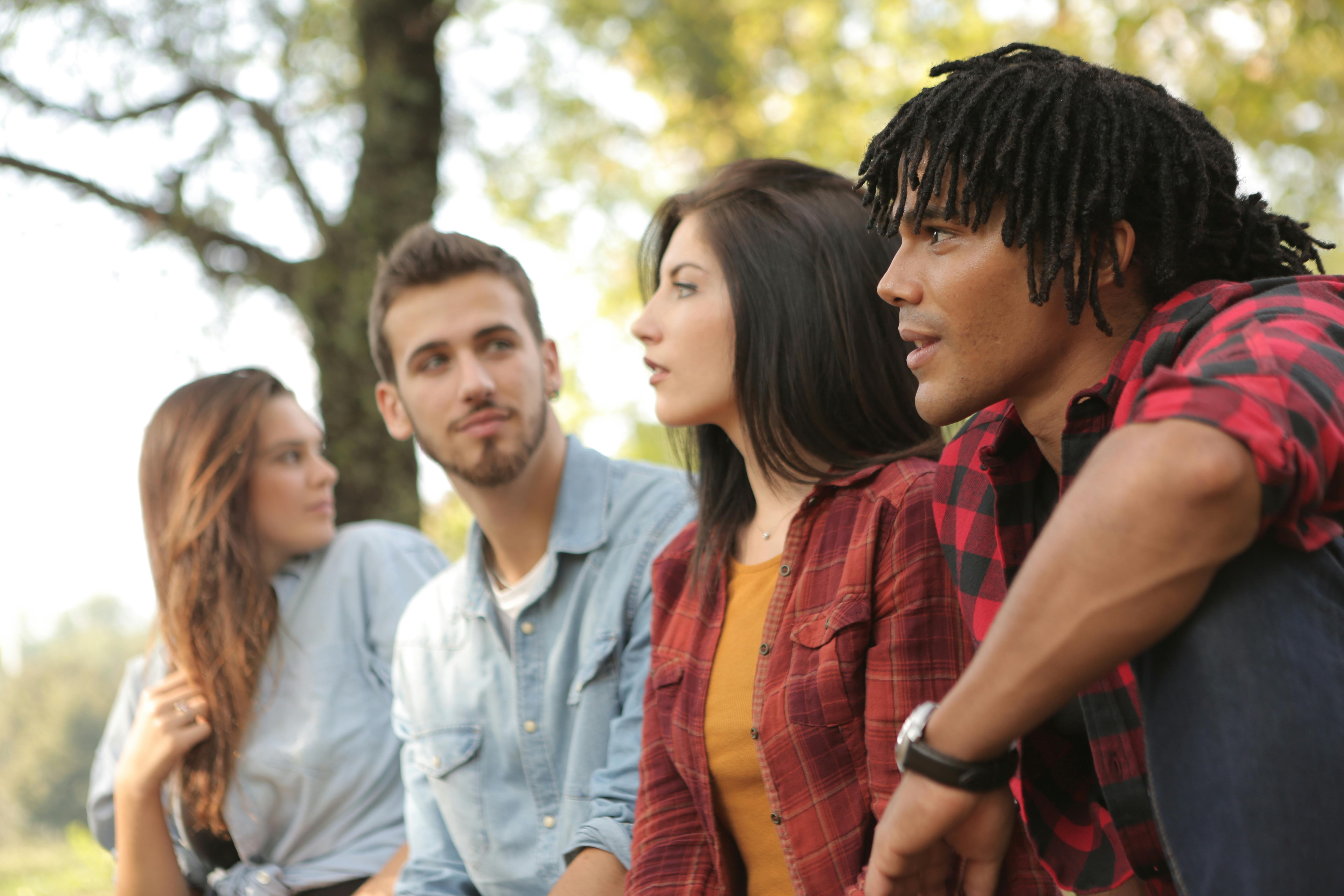 multiracial young people sitting in green forest