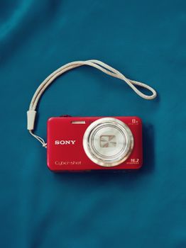 Top view of a red digital camera with strap on a blue background.