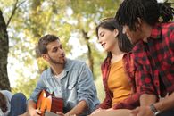 一个穿着牛仔的男人在公园里和朋友坐在一起弹吉他、唱歌