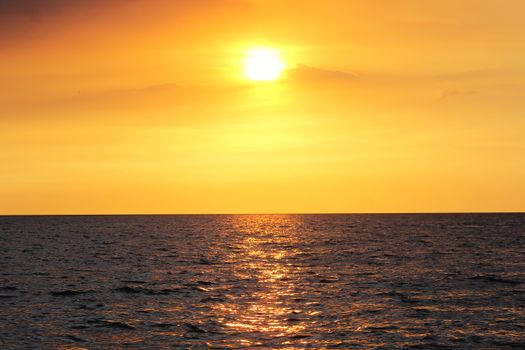 A breathtaking view of the ocean at sunset with a vivid orange sky and warm reflections on the water.