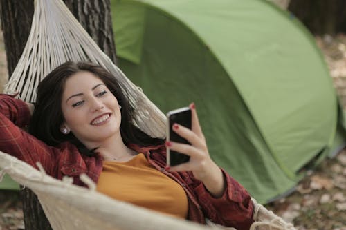 핸드폰을 사용하는 동안 해먹에 누워있는 여자의 사진
