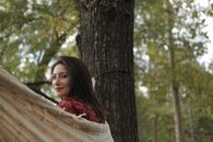 Side view of cheerful female chilling in hammock in green park while looking over shoulder at camera