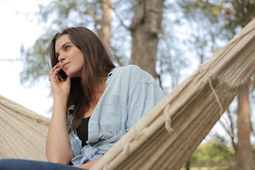 Free Woman Sitting on Hammock While Using Smartphone Stock Photo