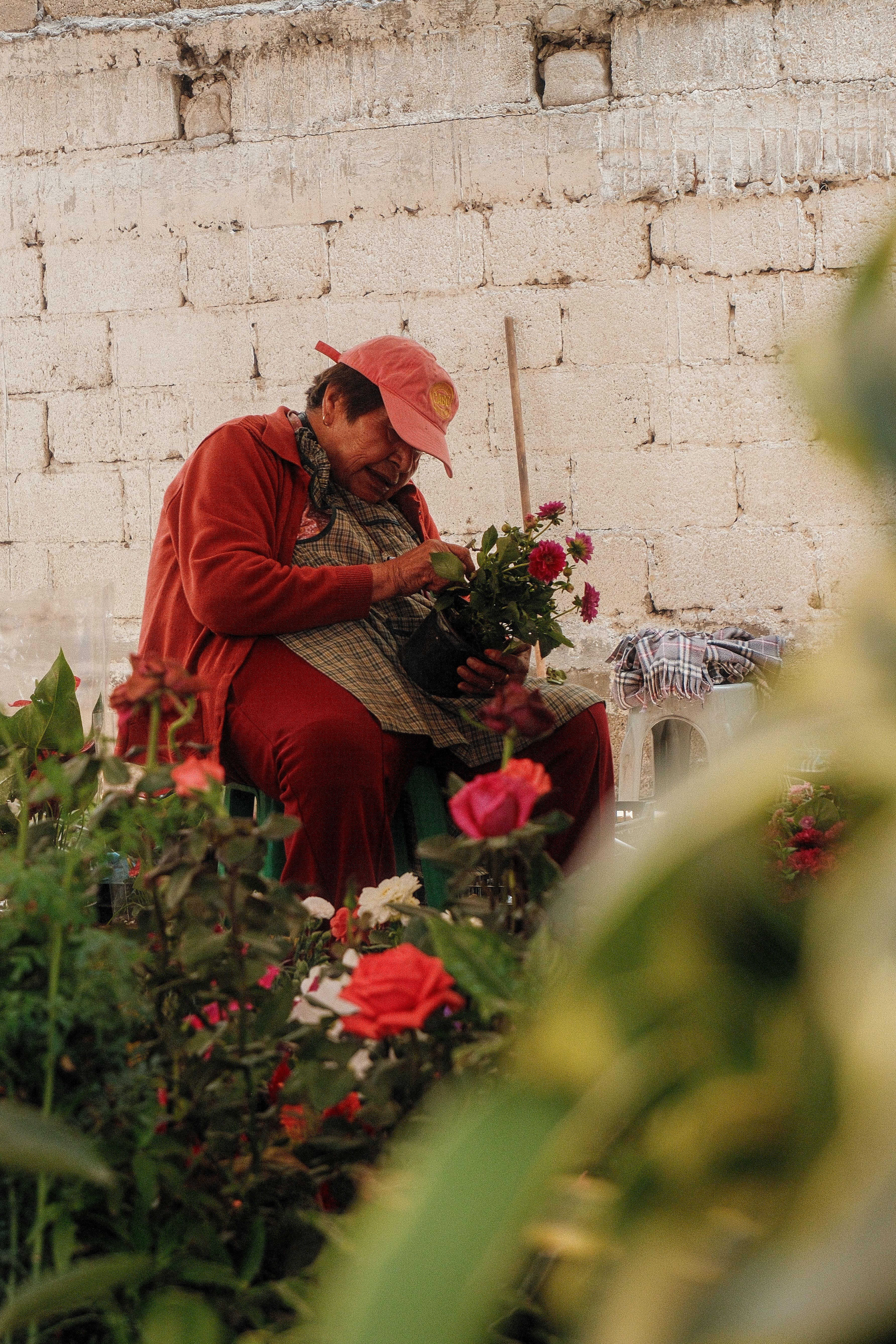 A flower vendor in a red outfit carefully arranges vibrant bouquets at an outdoor market.