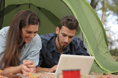 Happy couple resting in tent and surfing laptop while spending time together in park