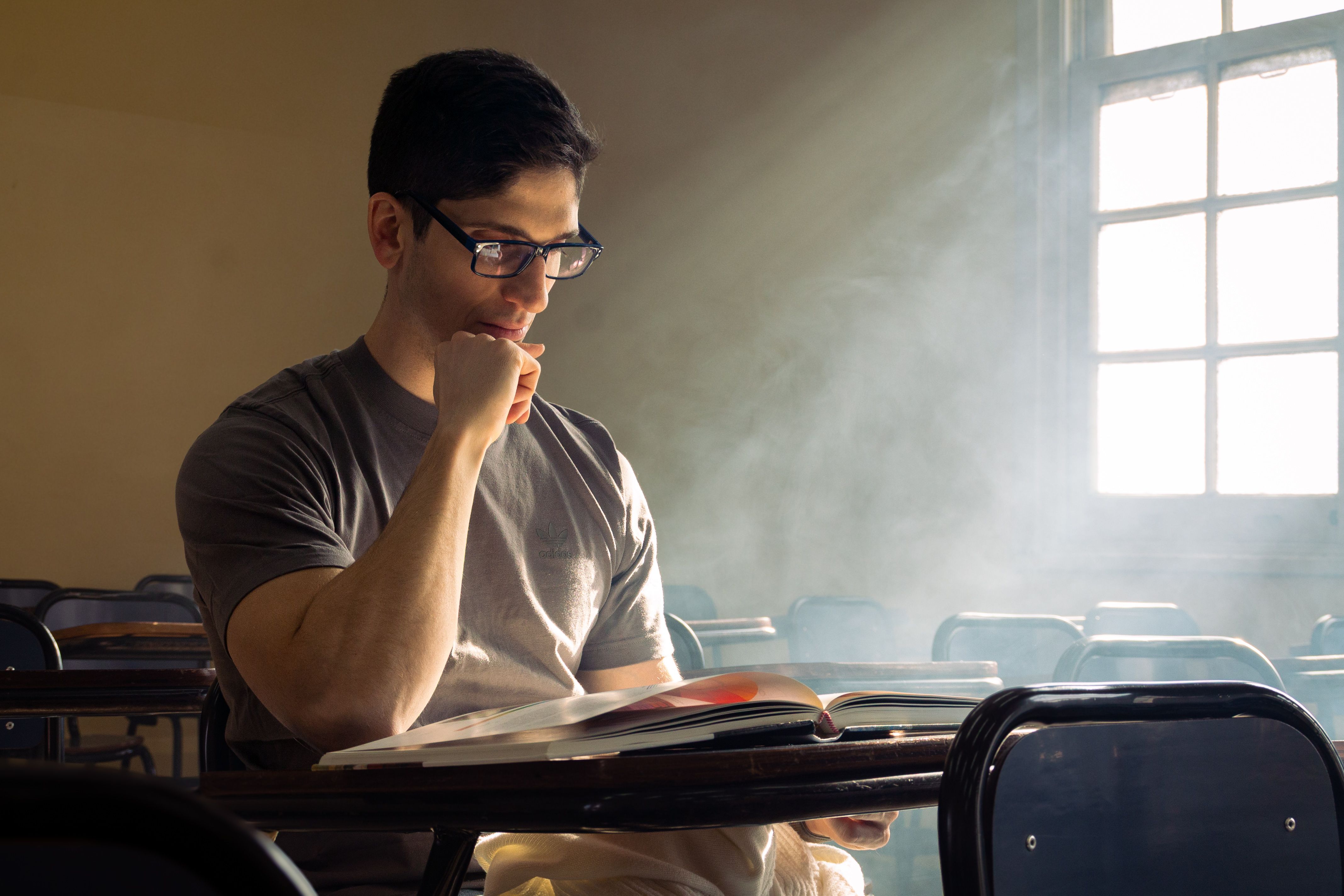 A young adult reading thoughtfully in a sunlit classroom creating moody atmosphere.