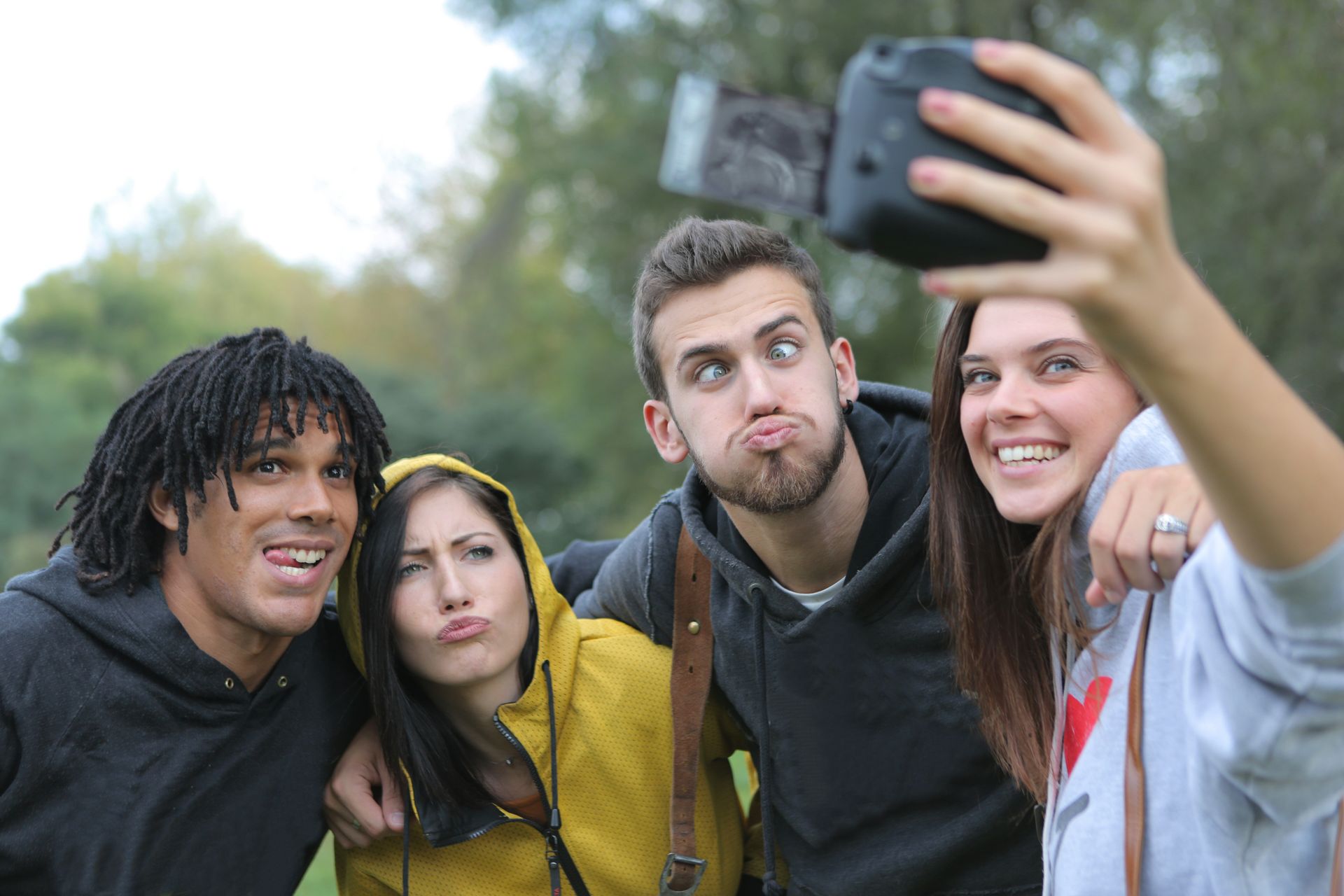 A group of friends capturing a wacky and joyful selfie moment in a green outdoor setting.