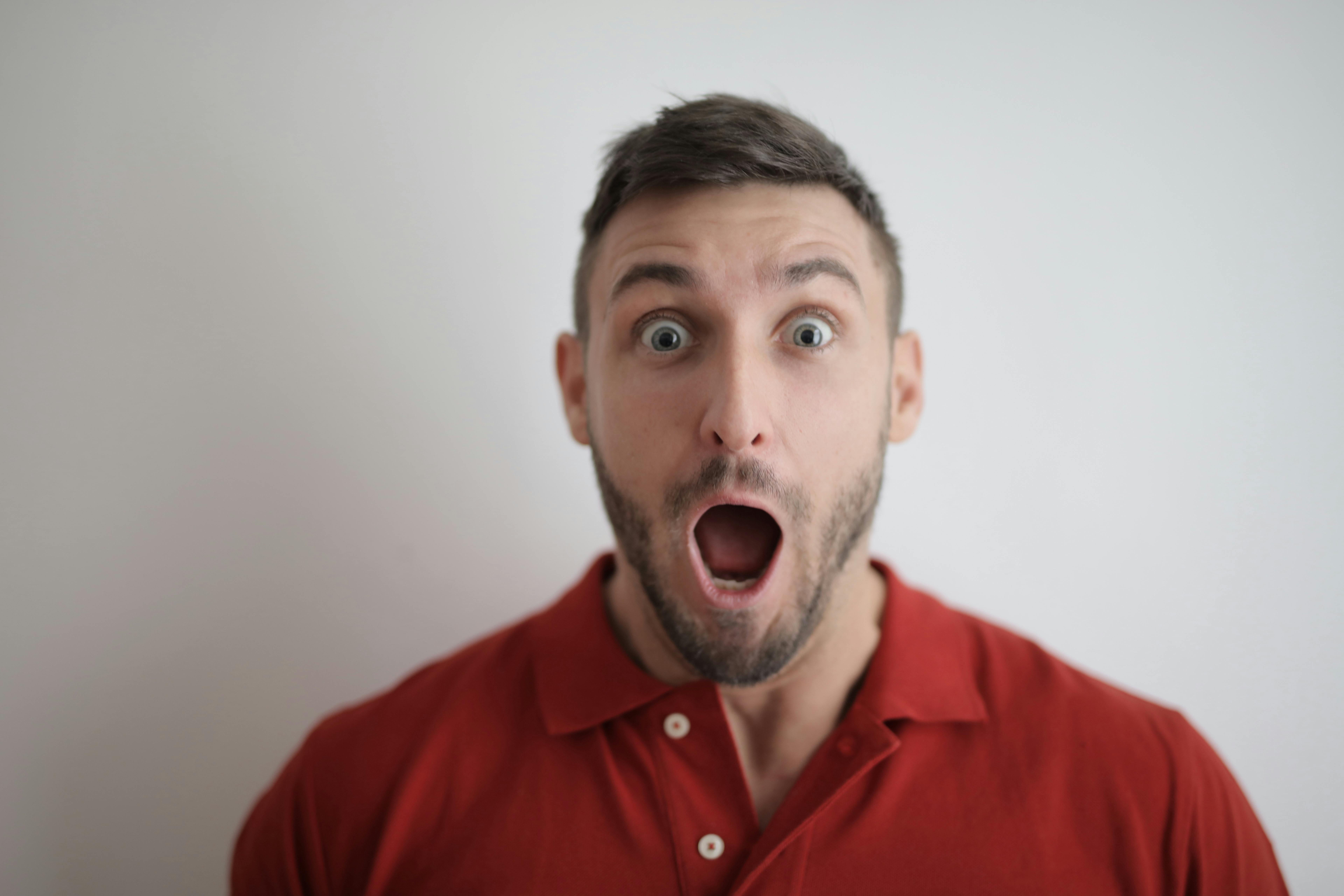 Shocked face of a man in red button up shirt. | Photo: Pexels