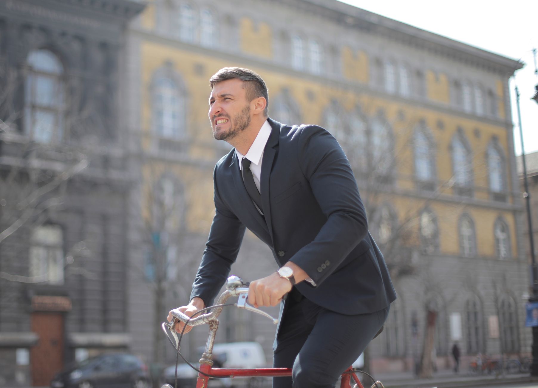 Man in formal attire cycling through a city street during the day.