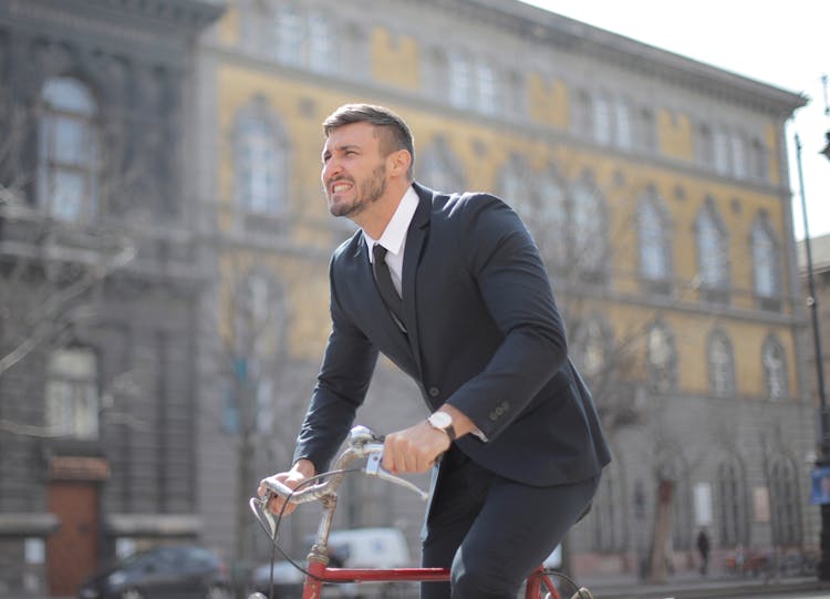 Man In Black Suit Jacket And Black Pants Riding On Red Bicycle