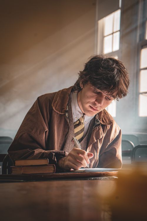 Free Young man writing in a sunlit classroom, focused on work. Stock Photo