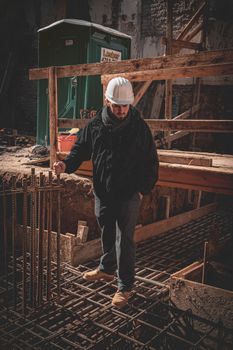 A construction worker in a hard hat inspects steel reinforcement bars on site.