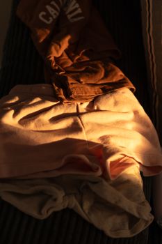 Warm sunlight casts a soft glow on folded clothing items, creating a cozy, serene ambiance.