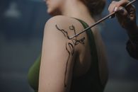 一位艺术家在女性肩膀上绘制的植物图案特写，展现了创造力和技巧