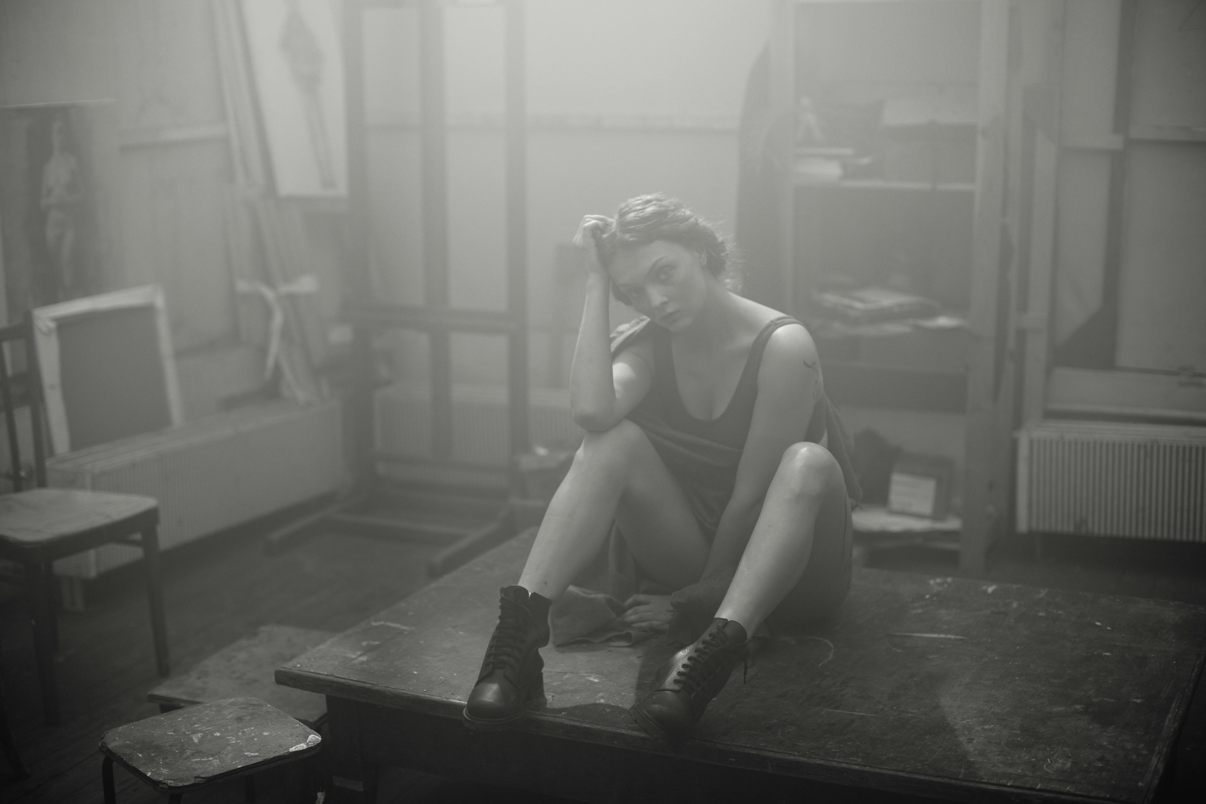 一位沉思的女人坐在工作室的桌子上，周围是雾蒙蒙的艺术环境