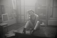 一位沉思的女人坐在工作室的桌子上，周围是雾蒙蒙的艺术环境