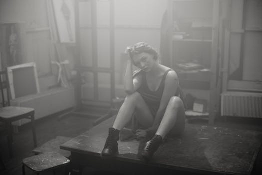 一位沉思的女人坐在工作室的桌子上，周围是雾蒙蒙的艺术环境