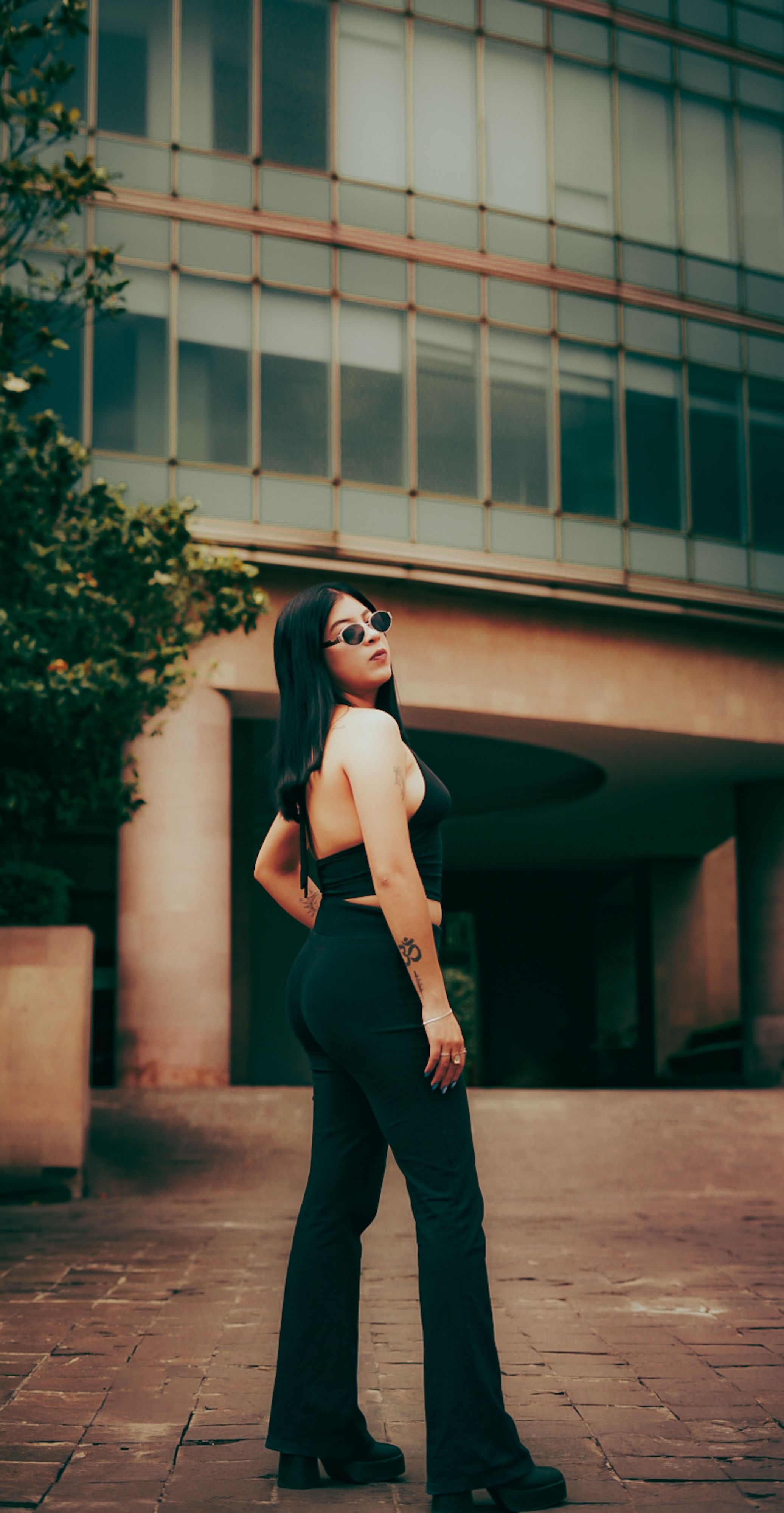 Mulher confiante em traje preto elegante posando do lado de fora de um prédio moderno, exibindo moda e estilo.