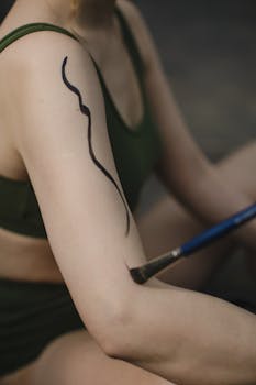 Close-up of artistic body paint on woman's arm with paintbrush.