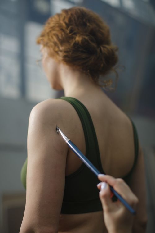 Free Close-up of a woman with a paintbrush held near her shoulder in a creative indoor environment. Stock Photo