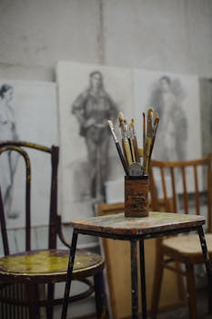A cozy art studio scene featuring paintbrushes and sketches on canvas chairs in the background.