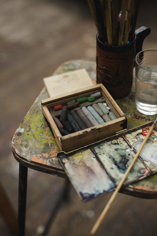 бесплатная Кисти для рисования на деревянном стуле рядом со стаканом воды Стоковое фото