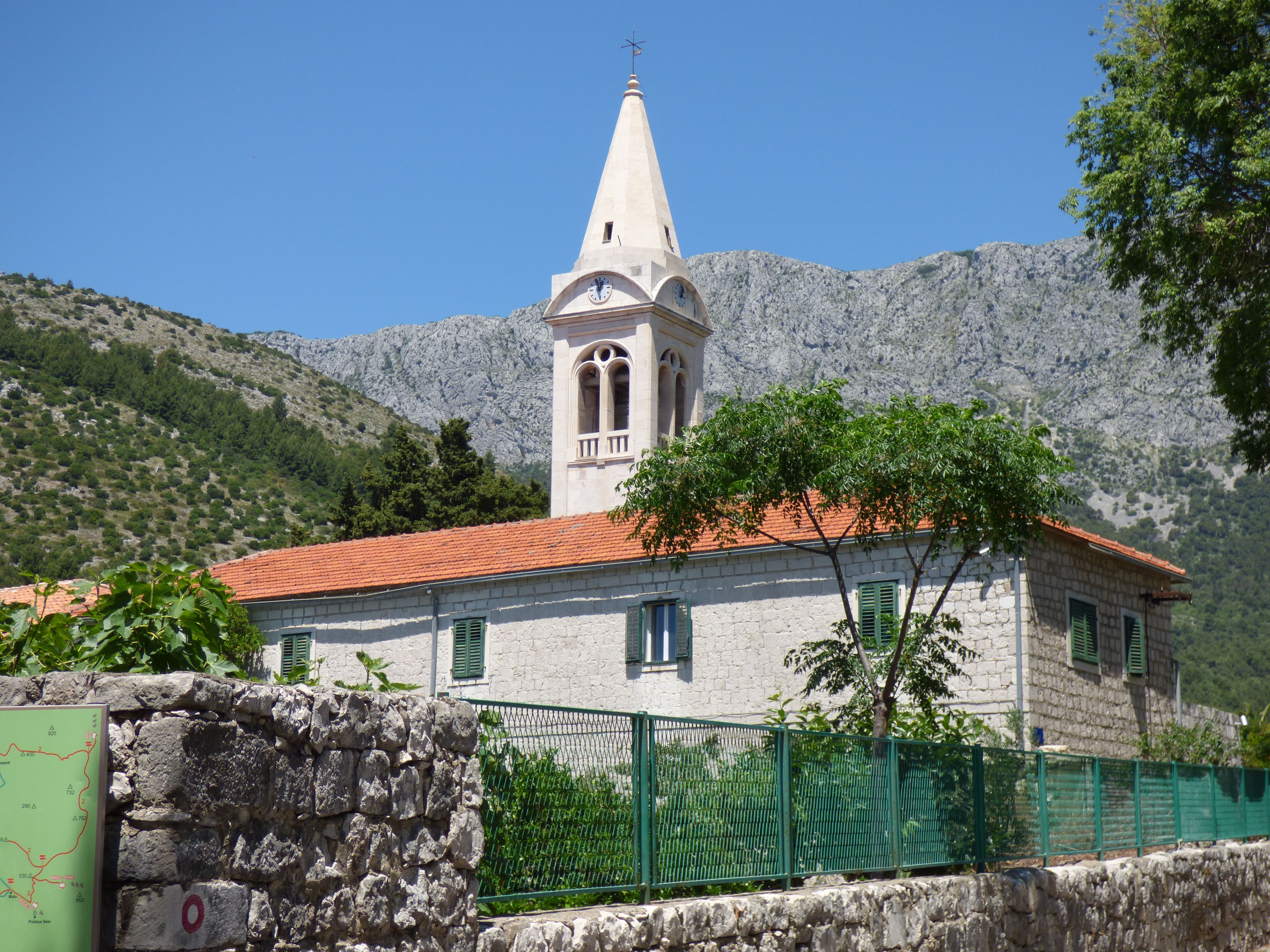 Beautiful church in Zaostrog, Croatia set against a mountain backdrop on a sunny day.