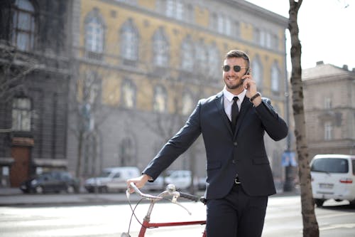 Man in Black Suit Jacket and Black Dress Pants Holding Red Bicycle