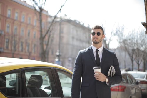 Free A confident businessman in a suit stands outdoors, holding coffee. Stock Photo
