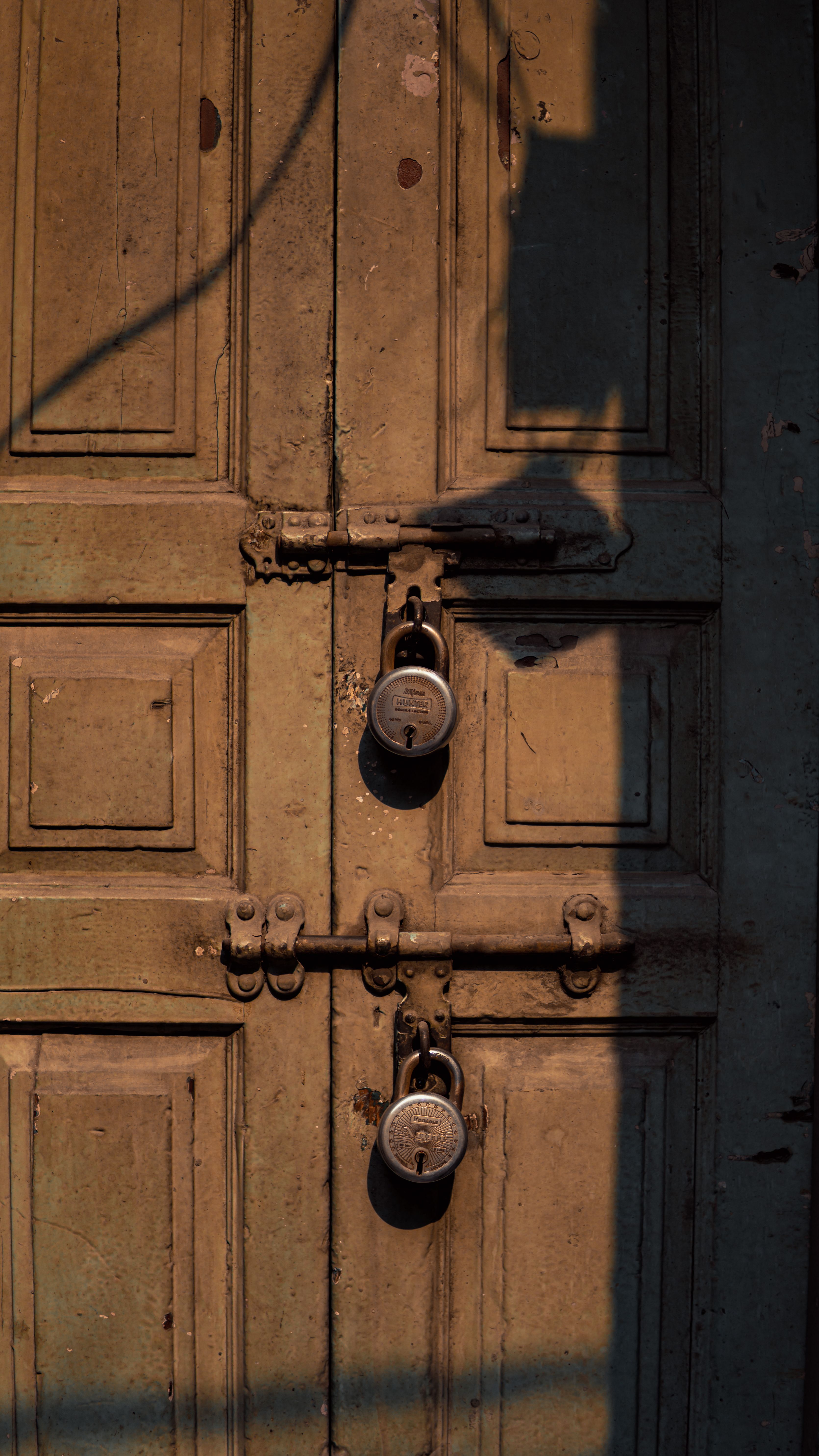 A rustic wooden door in Ludhiana, India, secured with padlocks, casting dramatic shadows.