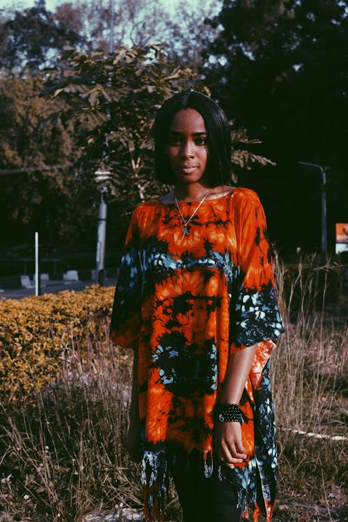 Young African American female with short hair wearing colorful dress looking at camera in park